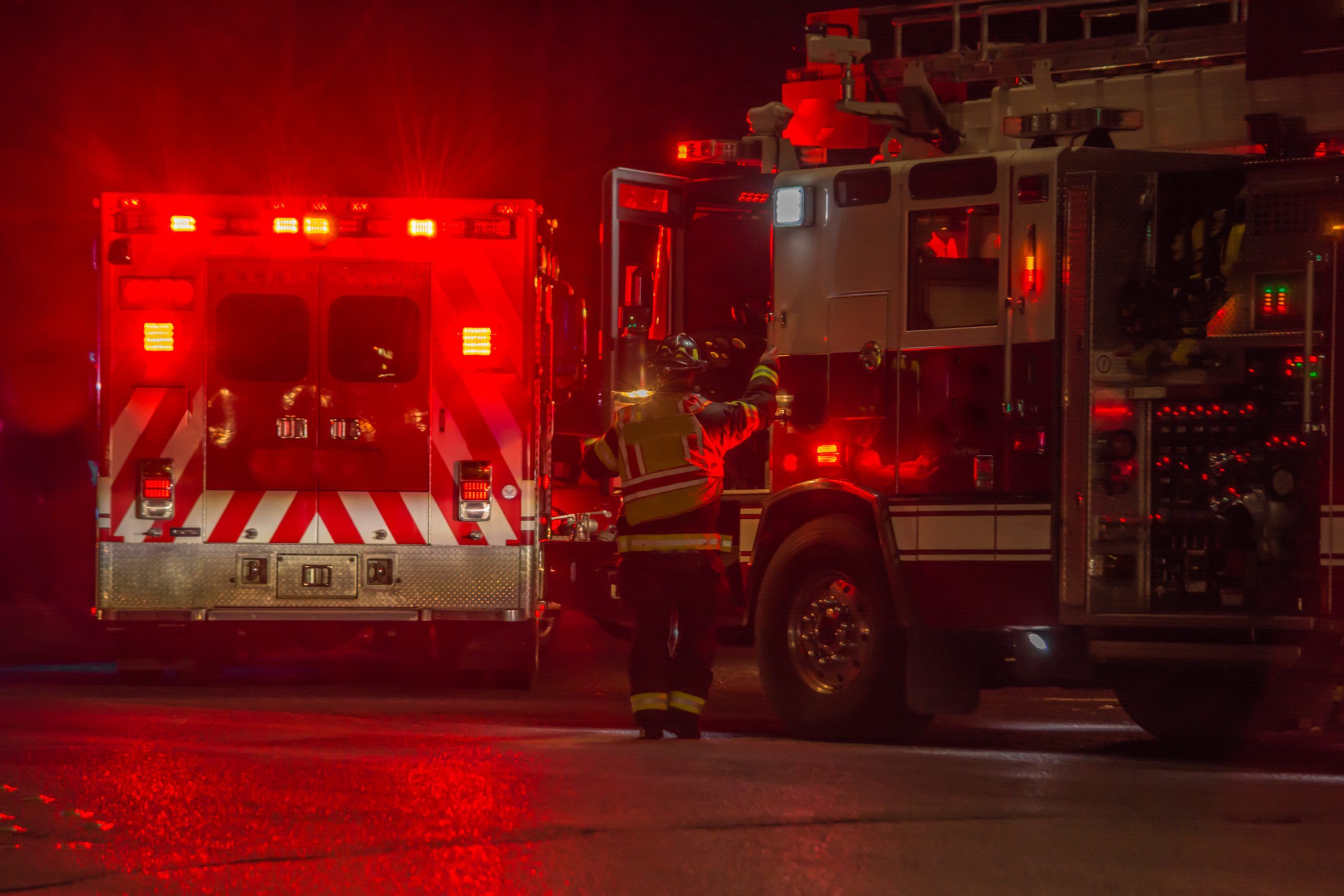 A firefighter enters a fire truck parked next to an ambulance